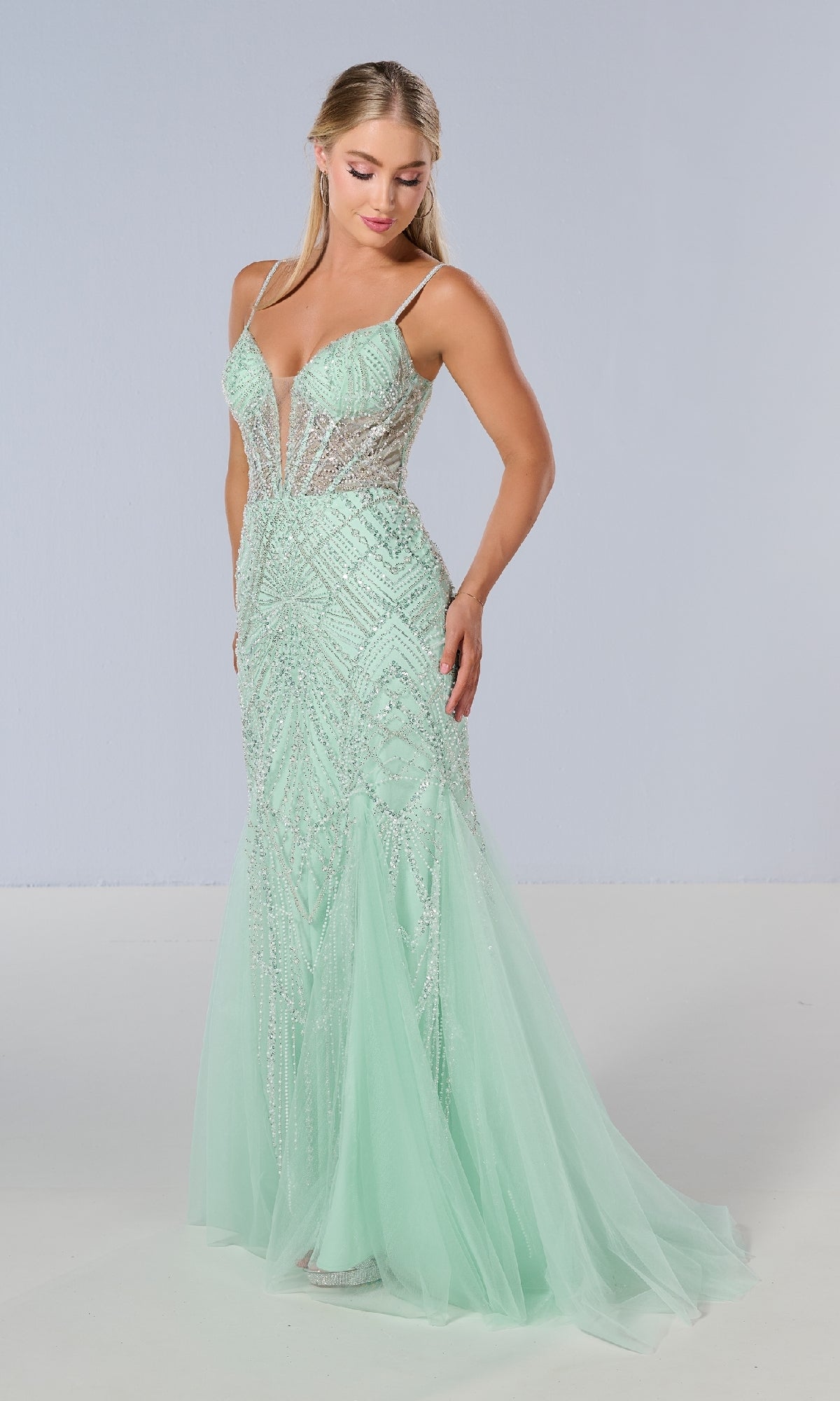 A woman models the Tiffany 16218 Long Prom Dress in mint green, featuring a sheer corset bodice with delicate beading, tulle accents, thin straps, and a deep V neckline against a plain light gray background.
